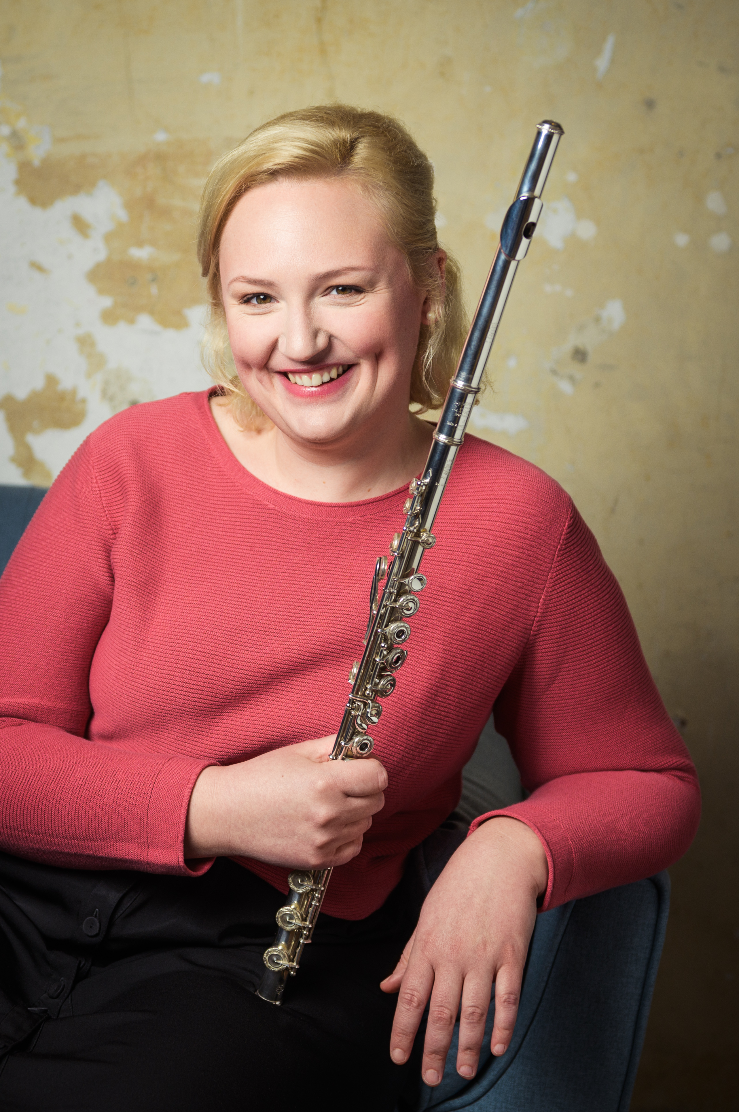 © Iveta Rysava Flötistin Katharina Sames sitzt auf einem Sofa und lächelt mit Querflöte in der Hand